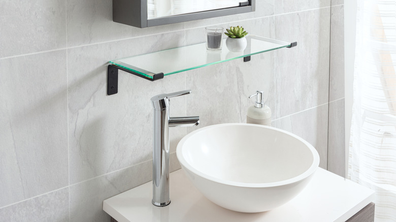 A round bathroom sink with a chrome faucet and glass shelf.