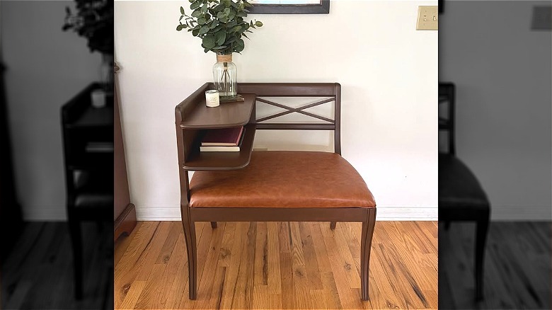 Wood gossip bench with brown leather seat, books, and a vase of greenery