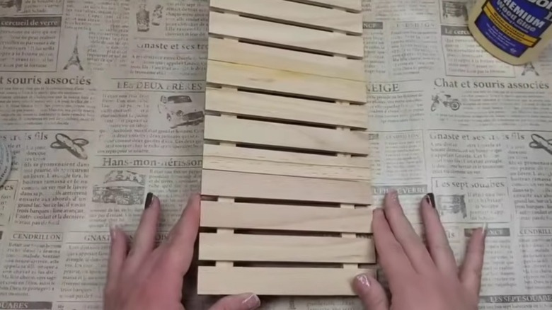 Person holding deconstructed Dollar Tree pallets on newspaper with wood glue bottle