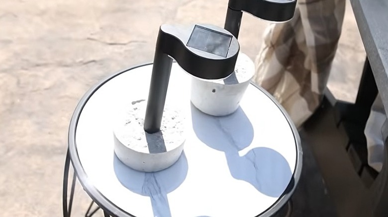 Two free-standing solar lights with their cement bases on a table outside