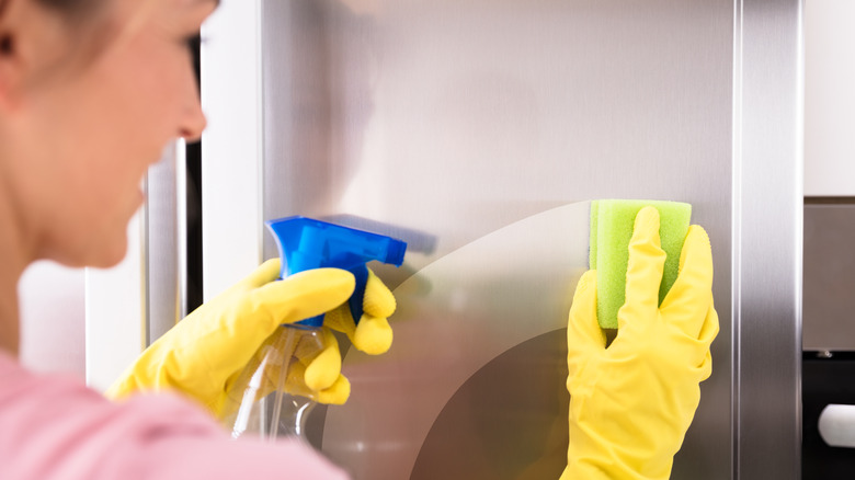 Woman cleaning stainless steel fridge