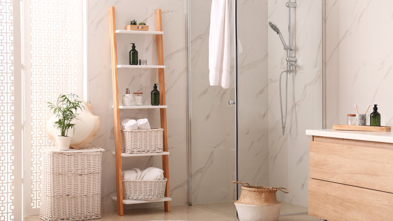 A neutral-colored bathroom with simple decor, including a ladder shelf and storage baskets