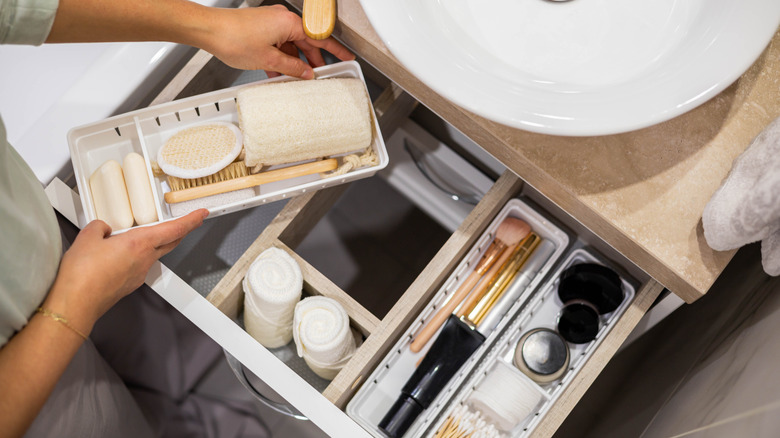 Person arranging storage bins containing personal care items in a drawer