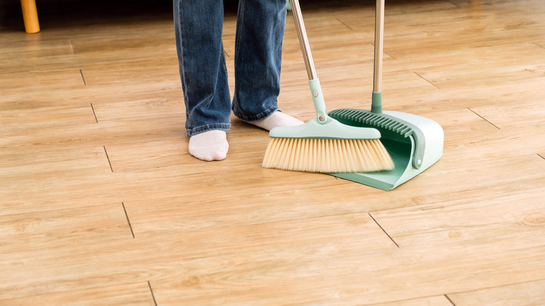 close up of person sweeping floors with broom and dust pan
