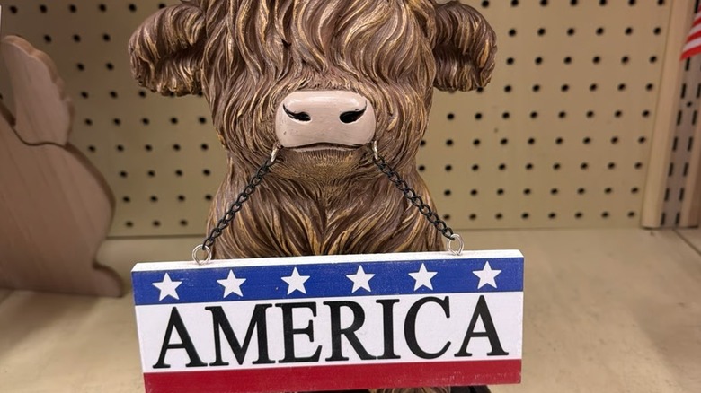 A highland cow figurine holding a sign in its mouth with America written on it.