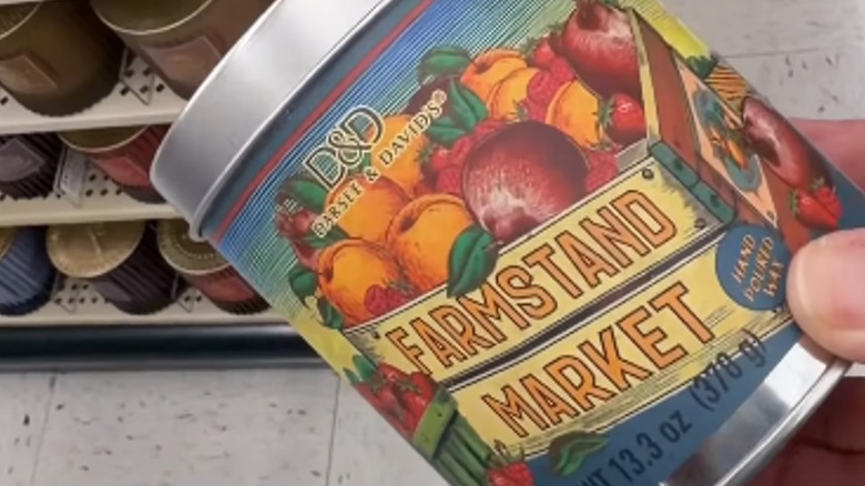 A hand holds a Farmstand Market tin candle from Hobby Lobby in the aisle of a store.