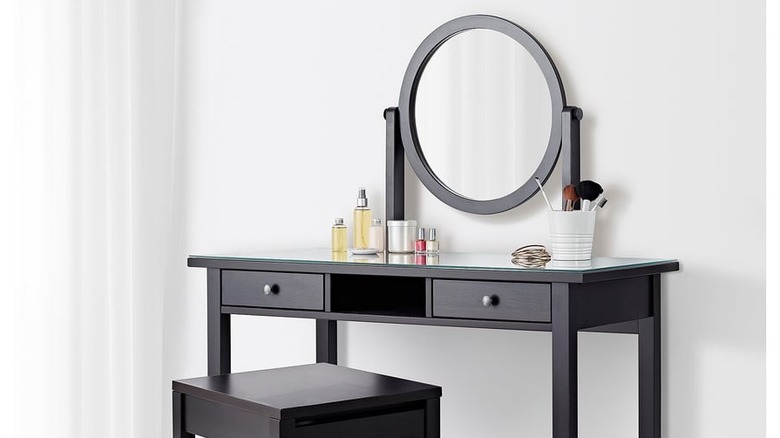 The HEMNES dressing table with mirror in the corner of a room with makeup brushes, perfumes, and other items on top