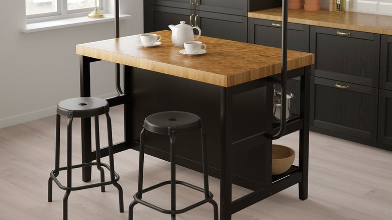 The VADHOLMA kitchen island with rack, with stools on one side and a tea pot and cups in the center