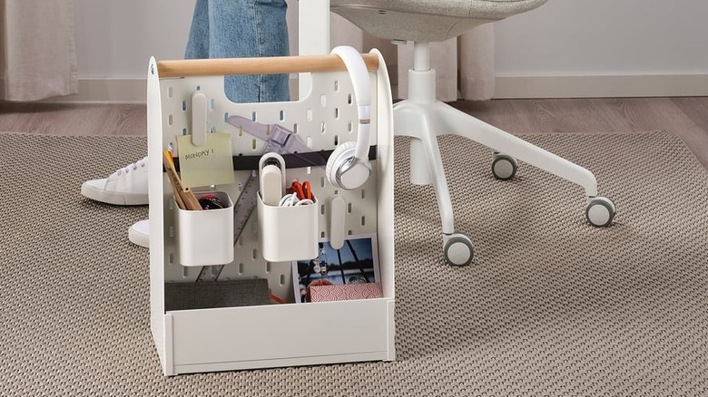 A VATTENKAR desk organizer filled with pencils, pictures, sticky notes, and even headphones on the floor next to someone sitting at a desk