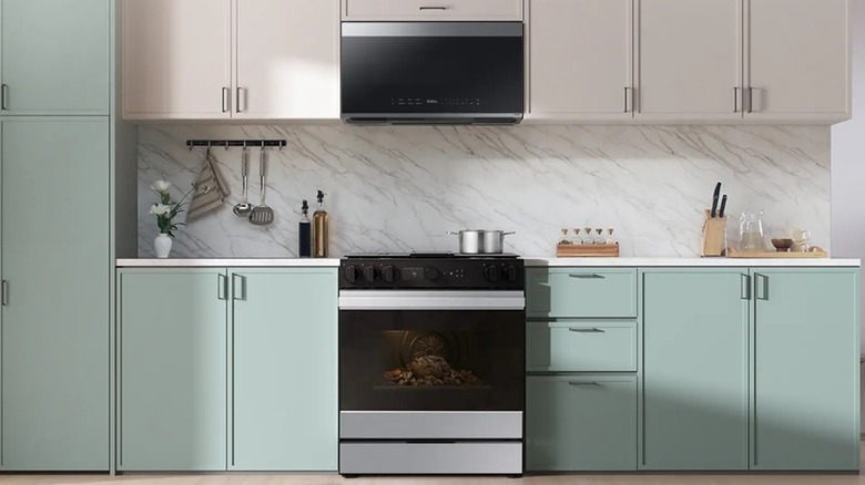 The Samsung Bespoke OTR Microwave in a kitchen with a Bespoke range, marble backsplash, and off white cabinets