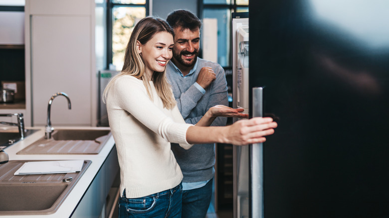 A happy couple looking at a refrigerator in a kitchen showroom together.