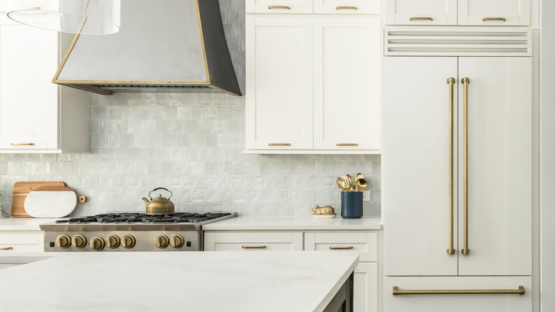 A white kitchen with white appliances and gold hardware.
