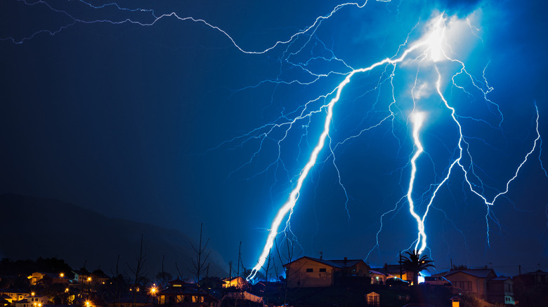 Cinematic bolts of lightning strike the ground behind a row of silhouetted houses.