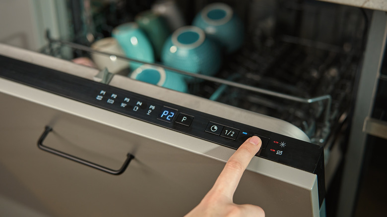 A partially opened dishwasher with a person's index finger pressing a button on the door.