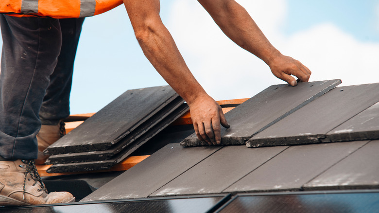 A construction worker installs slate tiles on a roof