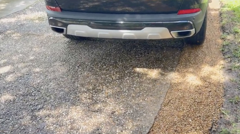 One tire of a car sits on a strip of gravel along the edge of a narrow driveway.
