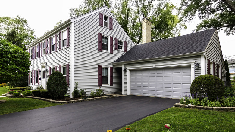 A narrow asphalt driveway in front of a traditional style home and garage painted white.