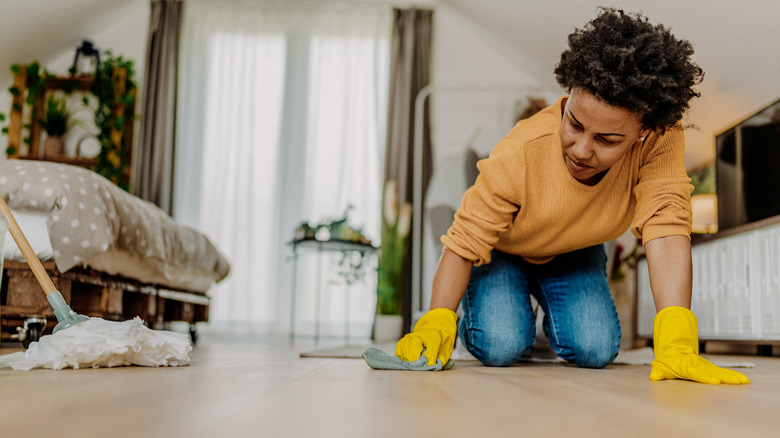 Woman wiping hardwood floor with cloth.