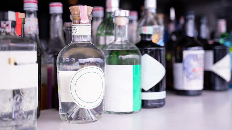 Glass bottles of alcohol lined up, including clear liquor in the forefront