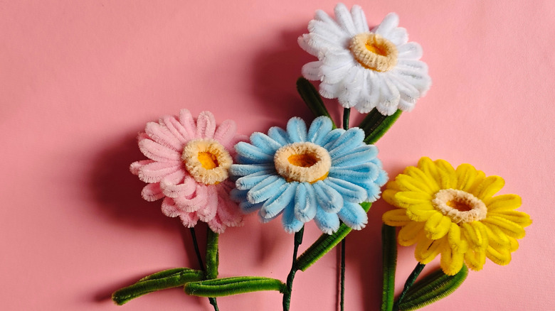 Handmade gerbera flowers crafted from colorful pipe cleaners arranged on a pastel pink background