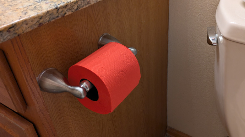 Red Renova toilet paper on a holder next to a toilet.