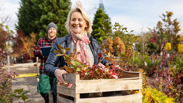 Woman carrying a crate of flowers on a fall day, a man in plaid behind her