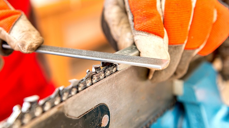 Close-up of gloved hands sharpening a chainsaw chain with file