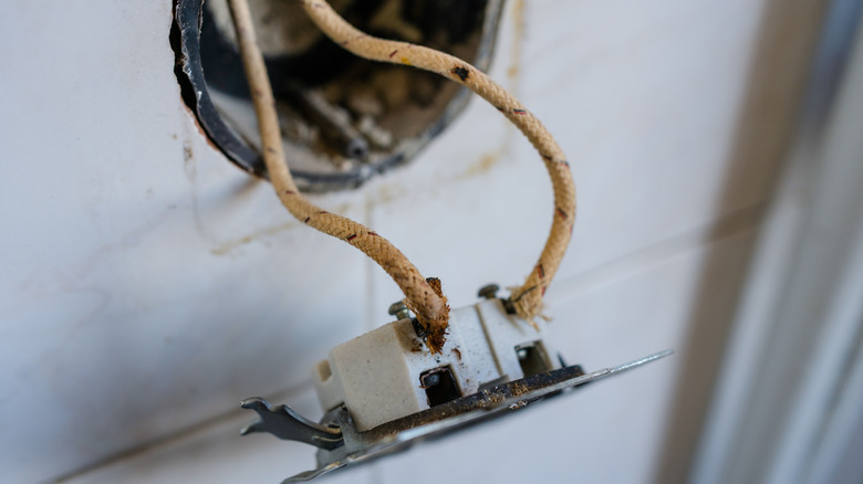 A wall socket hanging from a wall, exposing frayed cloth wires