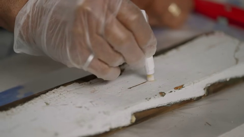 Gloved hand testing a painted wooden plank for lead paint