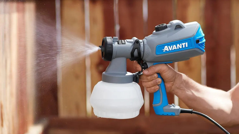 Person using Harbor Freight's Avanti spray gun to paint a fence