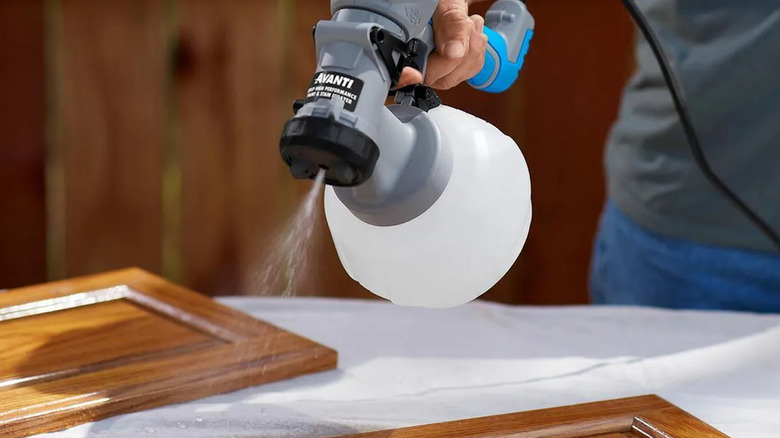 Person using Harbor Freight's Avanti spray gun to stain cabinet doors