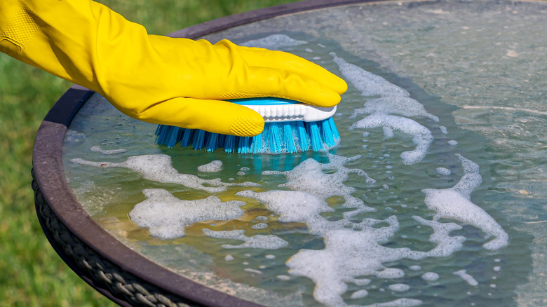 Person cleaning glass table with brush and soap.