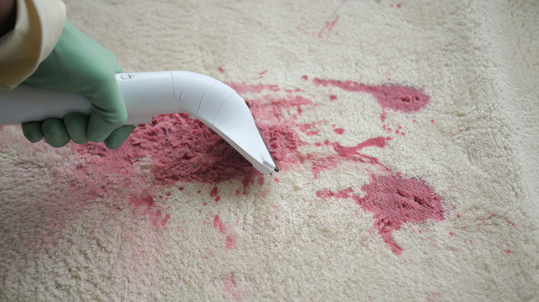 A green gloved hand steam cleaning a red stained cream carpet