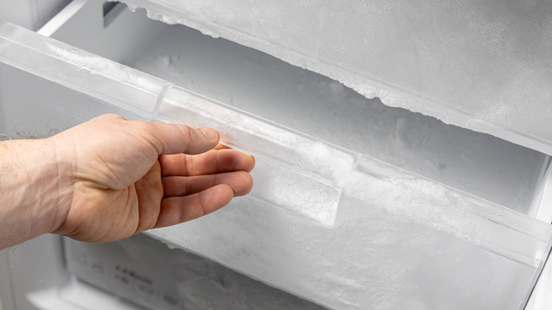 A hand pulling out a freezer drawer full of ice.
