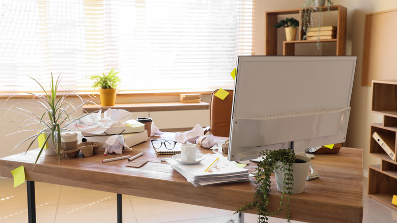 A messy office with random papers and trash over the desk and sticky notes everywhere
