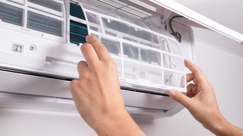 Two hands placing a filter back into a white wall-mounted AC unit