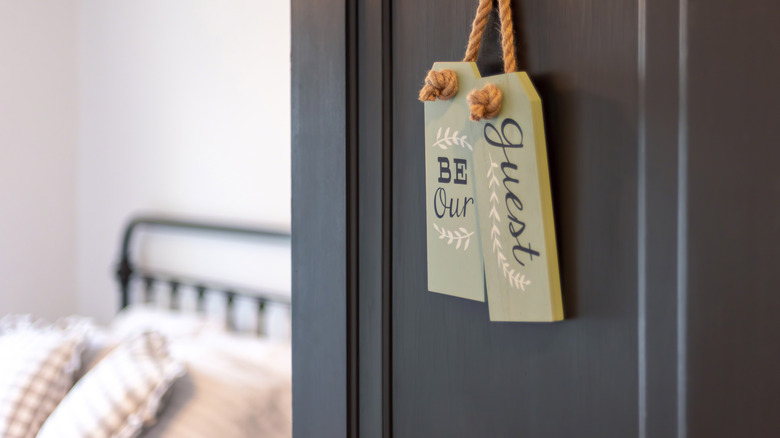 An open door leading into a bedroom with a sign saying "be our guest" hanging