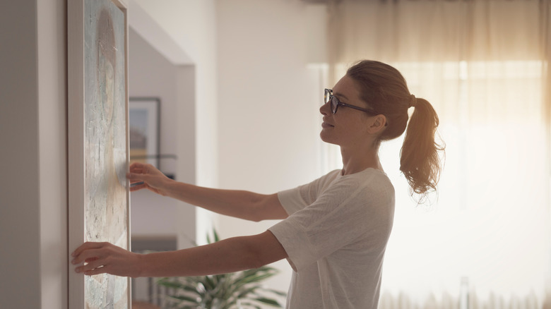 woman hanging painting on wall