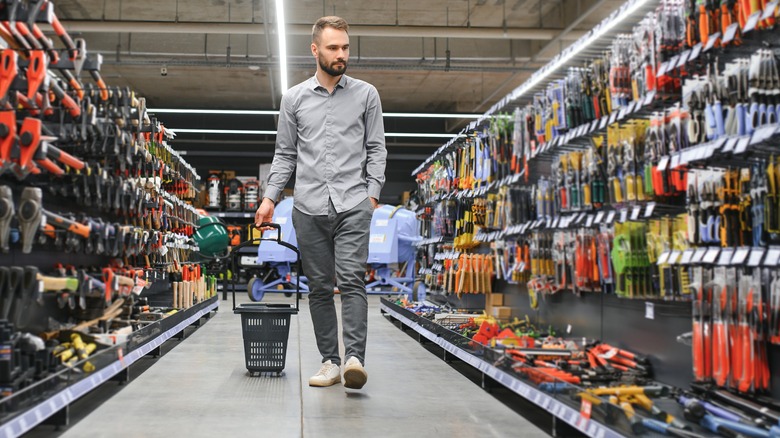 Man pulls a small basket with wheels behind him at the hardware store, planning to make a small purchase.