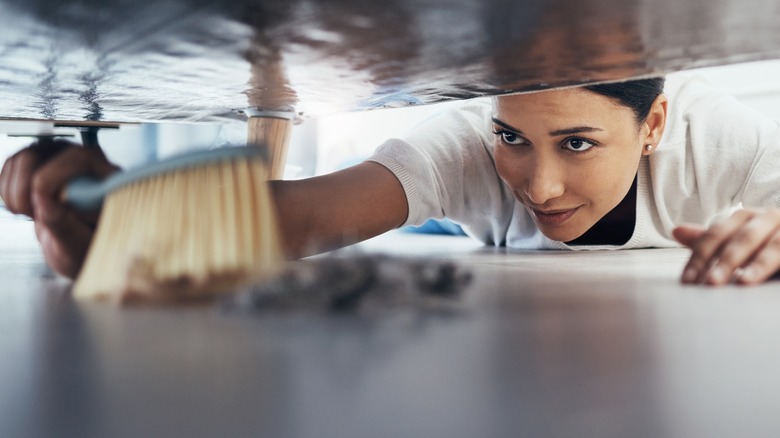 woman sweeping dust under sofa