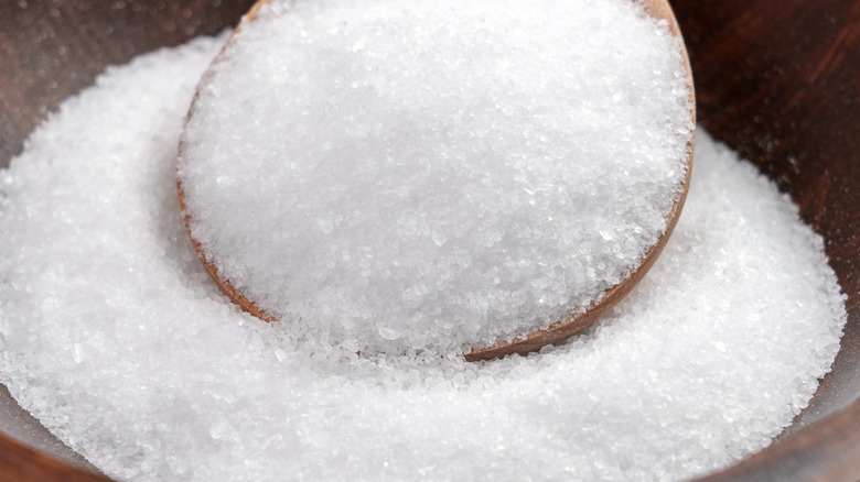 A close-up of white Epsom salt in a wooden bowl and spoon