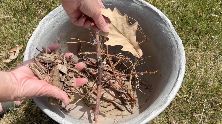 Person putting yard scarps into bottom of large planter as filler.