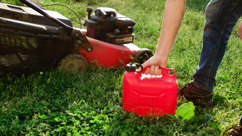 A man hold a gas canister next to a lawn mower