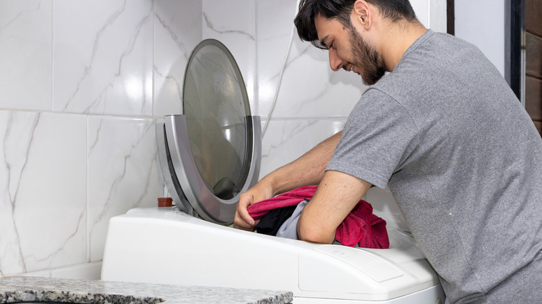 Man putting clothing in a top-load washing machine