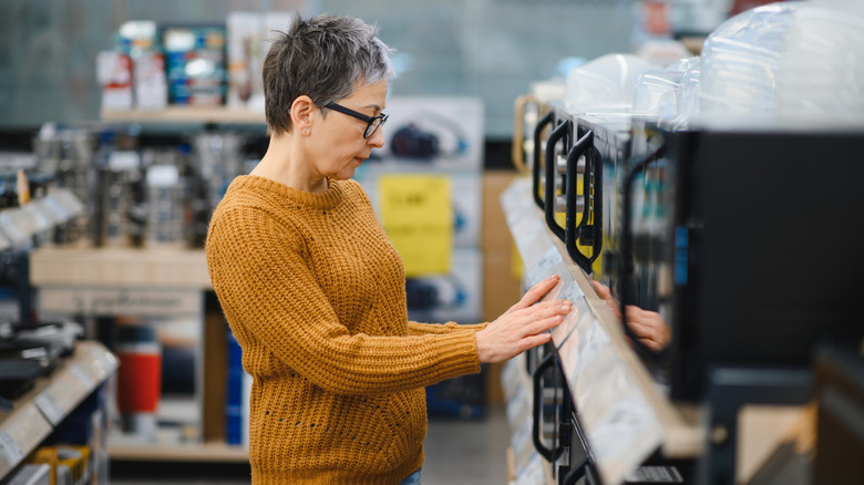 A woman in a yellow sweater looking at microwaves in an appliance store