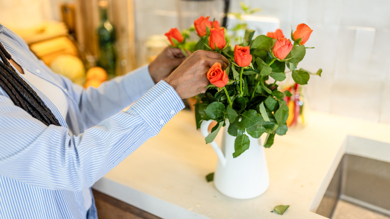 Woman arranging small orange roses in white pitcher