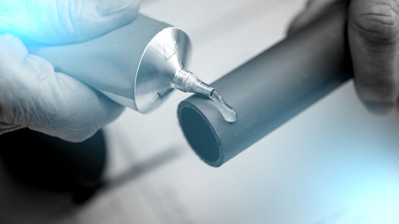 A person putting plumber's glue on the end of a pipe