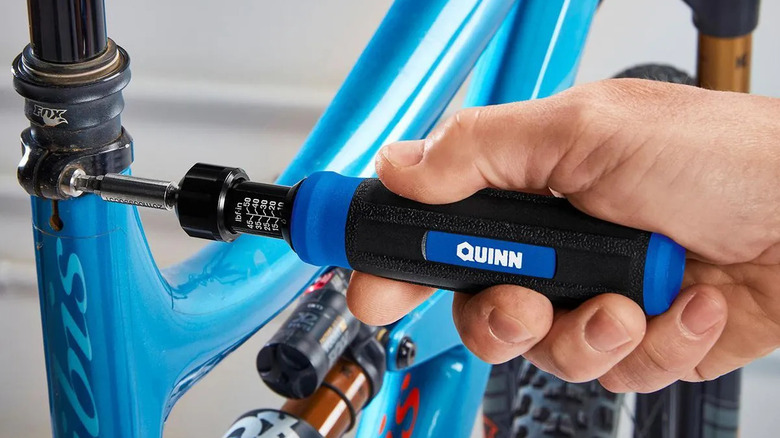 A hand is shown using a Quinn Precision Torque Screwdriver to tighten a screw