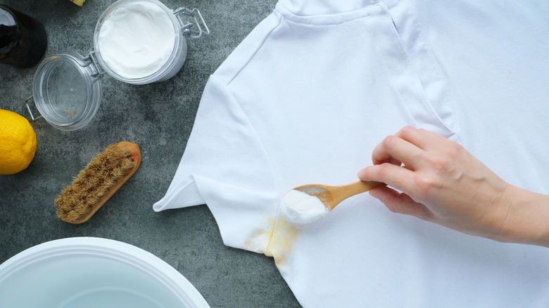 Person sprinkling baking soda on yellow sweat stain on white shirt