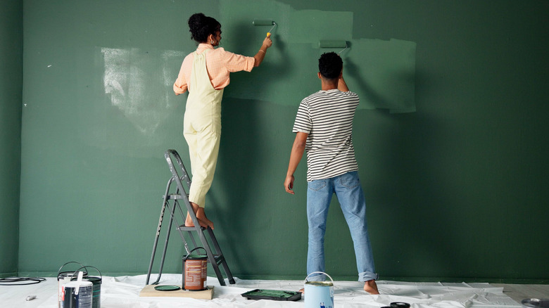 A couple is painting the walls of a room dark green together